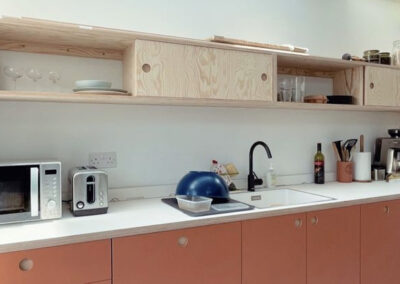 Plywood Kitchen in European Pine Ply and Teracotta laminate with bespoke plywood kitchen cupboards with sliding doors and recessed finger pull hand holes by The Life of Ply